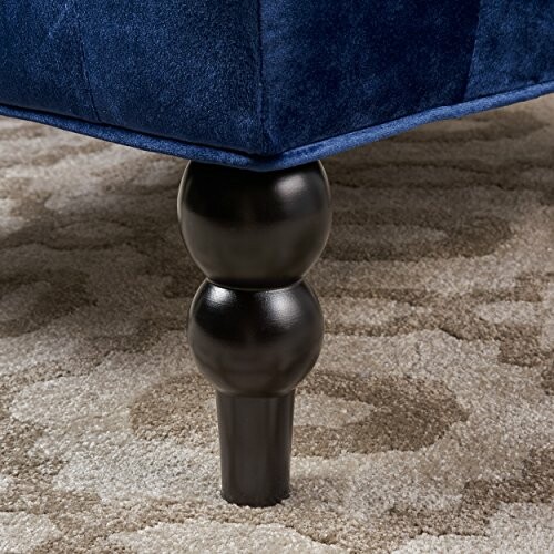 Close-up of a blue sofa leg on a patterned carpet.