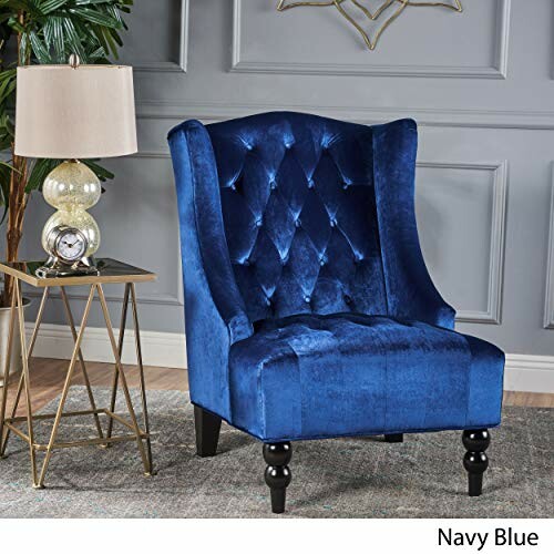 Navy blue velvet accent chair with tufted back next to a stylish lamp and side table.