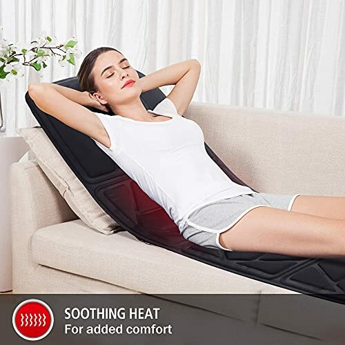 Woman relaxing on a couch using a heated massage pad.