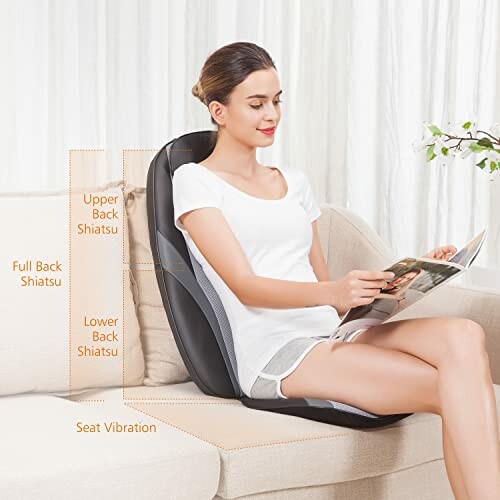 Woman sitting on a sofa using a massage cushion while reading a magazine.